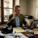 Un détective plongé dans ses dossiers, assis à son bureau encombré au cœur d’un vieux commissariat parisien.