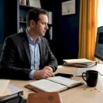 Dans son bureau, un détective privé scrute attentivement les informations affichées sur son écran d’ordinateur.