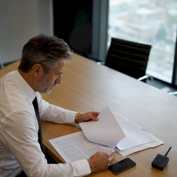 Un dirigeant en pleine réunion, attentif à son smartphone pour consulter ses messages importants.